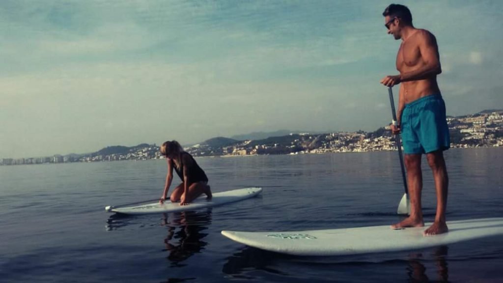 Dos personas en el mar encima de tablas de Paddle Surf en frente de El Palo haciendo una clase.