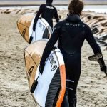 Dos chicos caminando por la playa con Tablas de Paddle Surf para olas