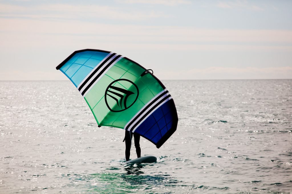 Una persona practicando el deporte de wingfoil con una cometa azul en el mar